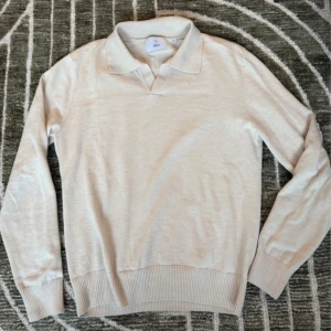 Beige pikétröja i ull från Bläck - Snygg beige pikétröja från Bläck i mjuk ull. Tröjan har klassisk krage, lång ärm och ribbade muddar vid ärmslut och nederkant. Perfekt för dig som gillar stilren och enkel design med en soft känsla.