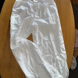 Vita linnebyxor från Gina Tricot - Snygga och luftiga vita linnebyxor från Gina Tricot med resår och snörning i midjan. Perfekta för varma dagar och chill stil. Byxorna har rak passform och är tillverkade i mjukt linnematerial för extra komfort.