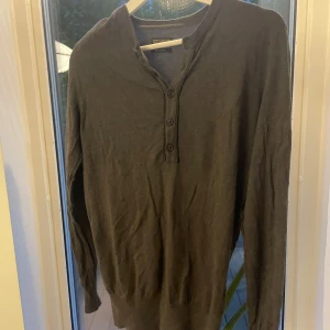 Mörkgrå långärmad tröja AllSaints - Säljer en mörkgrå långärmad tröja från AllSaints med knappar vid halsen. Tröjan har en avslappnad passform och är tillverkad i mjukt material, perfekt för lager på lager. Enkel och stilren design som funkar till det mesta.