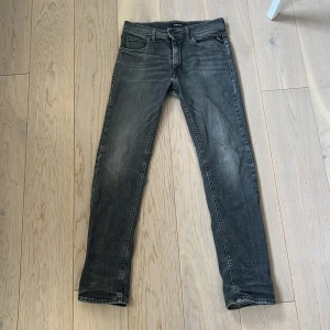 Replay grå straight fit jeans 12A - Snygga grå jeans från Replay i modellen Wallys. Jeansen har en straight fit passform, klassiska fem fickor och coola slitningar framtill. Perfekta för dig som gillar en smal siluett och vill ha ett par stilrena jeans med lite edge. Det är äkta köpta på Jeansbolaget i kungsmässan