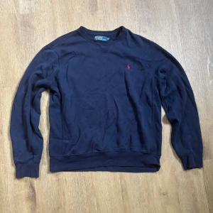 Mörkblå tröja från Polo Ralph Lauren - Snygg mörkblå tröja från Polo Ralph Lauren med klassisk rund hals och röd broderad logga på bröstet. Den är storlek M men passar också S.