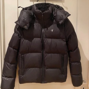 pufferjacka Calvin Klein Jeans M - Svart pufferjacka från Calvin Klein i mycket bra skick. Lite av loggan på armen har låstnat annars som ny. Jag är 177 och den är lite för liten för mig 