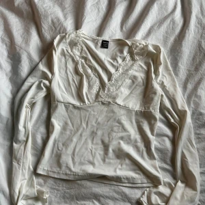 Vit långärmad topp med spets från SHEIN - Säljer en vit långärmad topp från SHEIN i storlek S. Toppen har en djup v-ringning med fina spetsdetaljer längs urringningen och är figurnära i modellen. 