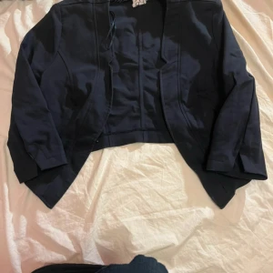 Svart kavaj från 2-Biz, stl 36 - Snygg svart kavaj från 2-Biz i storlek 36. Modellen är croppad med spetsiga kanter framtill och har långa ärmar. 