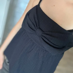 Mörkblå linnetopp med rosett från Kappahl - Supersöt mörkblå linnetopp från Kappahl med tunna axelband och en stor rosett framtill. Toppen har en lätt rynkad struktur och är luftig med en avslappnad passform. Perfekt för varma dagar när du vill ha något enkelt men ändå stilrent.