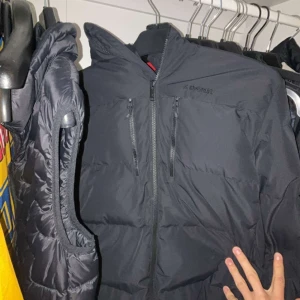 Svart pufferjacka från Everest - Svart pufferjacka från Everest med huva och två vertikala bröstfickor med dragkedja. Jackan har en clean look med diskret logga på bröstet och quiltad design. Perfekt för kalla dagar och har en normal passform.