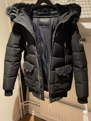 Svart pufferjacka Supply & Demand - Svart pufferjacka från Supply & Demand med stor huva och svart fuskpäls. S men funkar perfekt M.. Pälsen kan man ta av och sätta på genom en kedja.Perfekt för kalla dagar Speciellt inför vintern❄️