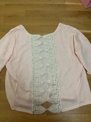 Ljusrosa topp med spetsdetalj i ryggen - Superfin ljusrosa topp med lös passform och trekvartsärm. ryggen har snygga spetsdetaljer 