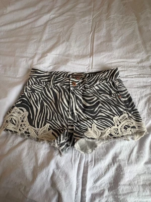 Zebramönstrade shorts med spets - Säljer ett par svarta och vita zebramönstrade shorts från Lab Industries i storlek 164. De har råa kanter och coola spetsdetaljer vid bensluten. Klassisk femficksmodell med knapp och dragkedja framtill💕