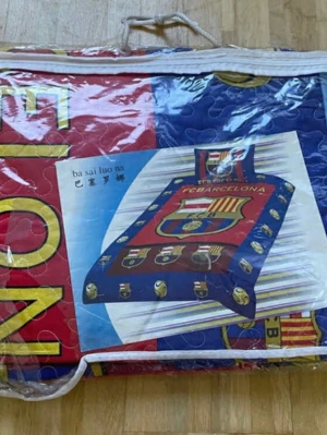 FC Barcelona quiltad väst - Säljer en quiltad väst med FC Barcelona-tryck i rött, blått och gult. Västen har ett stort klubbmärke framtill och coola fotbollsmotiv längs kanterna. Perfekt för dig som vill visa ditt lagstöd på ett unikt sätt. Materialet är polyester och designen är riktigt färgstark.