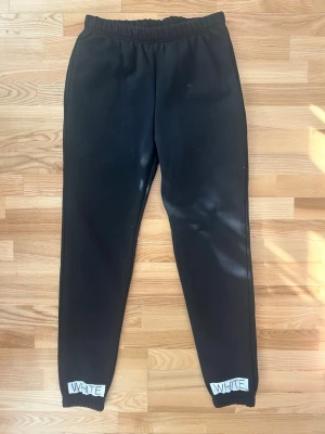 Off-White svarta mjukisbyxor med tryck - Svarta mjukisbyxor från Off-White med elastisk midja och vita diagonalränder på benen. Tryck med text och logga på framsidan samt 'WHITE' på bensluten. Tillverkade i 100% bomull för en skön och avslappnad känsla.
