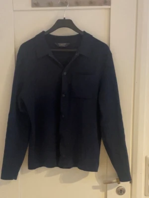 Mörkblå overshirt - Säljer en stilren mörkblå overshirt. Jackan har klassisk krage, knappstängning framtill och en bröstficka. Perfekt att slänga över en t-shirt för en clean look. Långärmad och i mjukt material. Storlek xs men passar som S