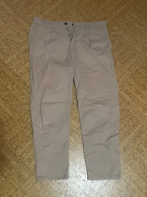 Beige chinos - Snygga beige chinos med tapered passform och klassisk midja. Byxorna har framfickor, bälteshällor och diskreta bakfickor. Perfekta för en chill och stilren look.