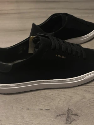 Axel Arigato - Clean 90 Suede Sneakers - Säljer ett par stilrena svarta sneakers från Axel Arigato med vit sula och diskret guldfärgad Axel Arigato logga på sidan. Skorna är helt oanvända bara testat sätta på högra skon. Skorna kommer i original förpackning med dust bag. Ny pris: 2 650