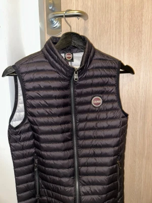 Svart dunväst från Colmar - Säljer en svart dunväst från Colmar Originals med quiltad design och dragkedja framtill. Västen har två fickor med dragkedja och Colmar-logga på bröstet. Perfekt för lager-på-lager och riktigt snygg till både hoodie och t-shirt. Använd men i bra skick. 164 men passar xs/xxs