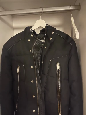 Svart pufferjacka från Horspist - Svart pufferjacka från Horspist med huva, stora silverfärgade dragkedjor och tryckknappar framtill. Jackan har emblem på ena ärmen och quiltad insida. Perfekt för kalla dagar och har en cool streetstil. Jackan är även i väldigt bra skick är andvänd bara 1 gång.Jackan funkar även i storlek M. Pris kan även diskuteras 