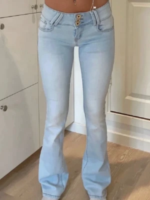 Ljusblå bootcut jeans med hög midja - Snygga ljusblå jeans med bootcut och hög midja. Jeansen har tre knappar framtill, klassiska fickor både fram och bak samt en mjuk och stretchig jeanskvalitet. Passformen är slim upptill och vidare nedtill, vilket ger en trendig siluett.