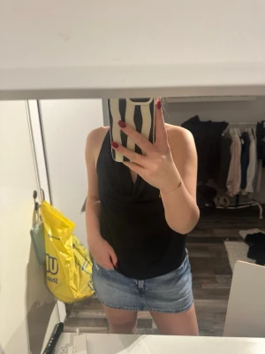 Svart halterneck topp - Säljer en svart  halterneck topp med snygg drapering framtill och öppen rygg. Toppen har breda band som knyts i nacken och är ärmlös