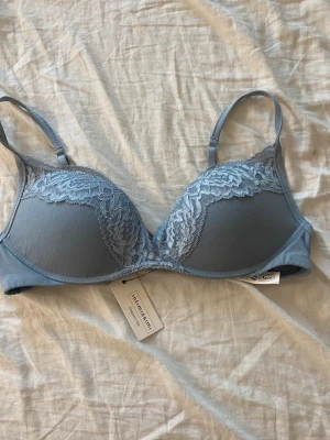 Blå spetsdetaljerad bh från Intimissimi - Snygg blå bh från Intimissimi med vackra spetsdetaljer över kuporna. Bh:n har justerbara axelband och en mjuk, slät yta som ger en bekväm känsla. Perfekt för dig som gillar stilrena underkläder med en touch av elegans.