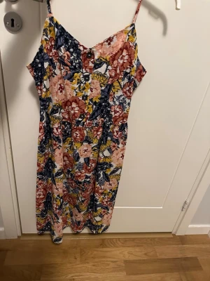Blommig långklänning från Esmara - Säljer en färgglad långklänning från Esmara i storlek 40. Klänningen har smala axelband, v-ringad front och ett blommigt mönster i blått, rött, gult och vitt. Materialet är 55% linne och 45% bomull, vilket gör den både luftig och bekväm. Perfekt för varma dagar! aldrig använd dock tvättad en gång :)