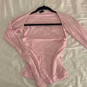 Ljusrosa topp från Gina Tricot - Säljer en ljusrosa topp från Gina Tricot i mjukt och stretchigt syntetmaterial. Toppen har långärmade bolerodetaljer och är figurnära. Knappt använd. 