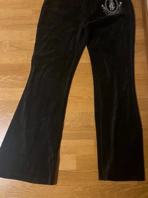 Y2K Juicy Couture - Säljer ett par svarta velourbyxor från Juicy Couture i storlek S. Byxorna har bootcut-modell, snörning i midjan och emblem med palmer och logga på ena benet. Var tvungen att sälja dem då jag gick ner drastiskt i vikt. Pris lapp helt nya. Ordinarie pris 1599-1299kr.