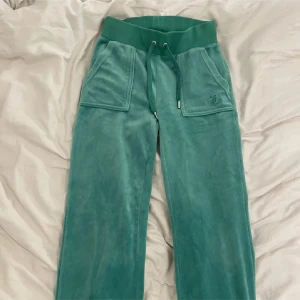 Turkosa mjukisbyxor Juicy Couture XXS - Säljer ett par turkosa mjukisbyxor från Juicy Couture i storlek XXS. Byxorna har bred resårmidja med snörning, stora fickor fram och bak med knappdetaljer samt broderad logga på ena fickan. Mjukt och skönt material som ger en chill vibe.