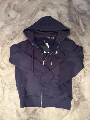 Polo Ralph Louren tröja - Marinblå zip-hoodie från Polo Ralph Lauren med huva, dragkedja och broderad logotyp på bröstet.