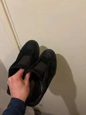 Svarta sneakers från Axel Arigato - Stilrena svarta sneakers från Axel Arigato i mocka med diskret logga i guld på sidan. Skorna har en klassisk låg profil och platt sula, perfekt för en clean och modern.