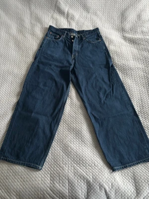 Weekday astro baggy jeans - Säljer ett par mörkblå jeans från Weekday, modell Astro. De har breda ben, hög midja och klassisk femficksdesign. Jeansen är tillverkade i bomull och har knäppning med silverfärgade knappar framtill. Storlek: W30 L30. OBS storleken som jag skrivit är den som gäller, inte 38!