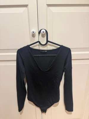 Svart långärmad body med v-ringning - Säljer en svart body från Stradivarius med lång ärm och djup v-ringning. Tillverkad i mjuk bomullsmix och har knäppning nedtill. 