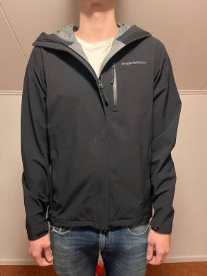 Svart vindjacka Peak Performance S - Peak Performance Xenon vindjacka i svart med huva och vattentätt HIPE-material. Jackan har dragkedja fram, bröstficka med dragkedja och diskret logga på bröstet. Perfekt för blåsiga dagar och outdoor-aktiviteter. Snygg och funktionell design. Inga defekter och använd få tal gånger.