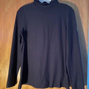 Marinblå polotröja i bomull - En stilren polotröja med lång ärm och klassisk hög krage. Tröjan är tillverkad i mjuk bomull och passar perfekt för lager-på-lager under kyliga dagar. Enkel och tidlös design som funkar till många olika outfits.