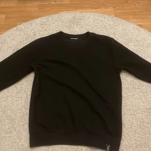 Svart tröja från Kappahl - En stilren svart tröja från Kappahl i storlek 158/164. Tröjan har rund hals, långärmade ärmar och en enkel design utan mönster eller detaljer. Perfekt för dig som gillar en clean och klassisk look.