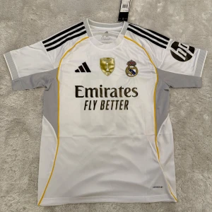 Real Madrid Mbappé 10 matchtröja Adidas - Snygg Real Madrid fotbollströja med Mbappé och nummer 10 på ryggen. Vit med svarta detaljer, guldiga inslag och gula linjer. Adidas-logga, klubbmärke och sponsortryck framtill. Tillverkad i lätt och ventilerande material.