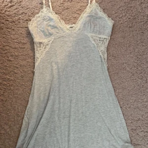 Vit kortklänning med spetsdetaljer - Supersöt vit kortklänning med tunna axelband och v-ringad hals. Klänningen har fina spetsdetaljer vid byst och sidorna som ger en romantisk vibe. Materialet är mjukt och lätt, perfekt för varma dagar. Passformen är normal och klänningen är ärmlös.