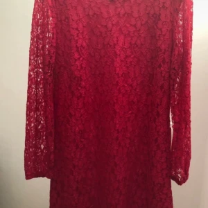 Röd spetsklänning med lång ärm - Säljer en röd kortklänning med lång ärm i vacker spets. Klänningen har ett blommigt spetsmönster som ger en romantisk vibe och är lätt transparent i ärmarna. Perfekt för dig som vill sticka ut med färg och detaljer.