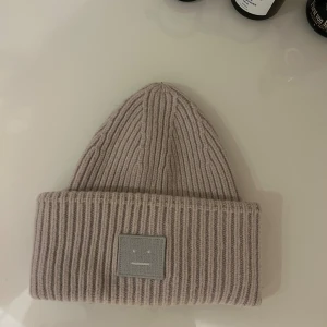 Beige ribbstickad mössa Acne Studios - Ribbstickad beige mössa från Acne Studios med bred uppvikt kant och det ikoniska ansiktsloggan framtill. Tillverkad i mjuk ull som håller dig varm.