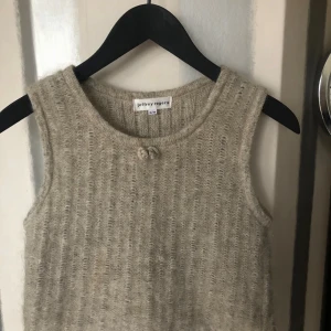 Beige stickad topp Jeffrey Rogers - Supermysig beige stickad linnetopp från Jeffrey Rogers i storlek S/M. Toppen är ärmlös och har en rund halsringning med en liten knutdetalj framtill. Materialet är en lyxig mix av mohair, ull och polyester som ger en fluffig och mjuk känsla.