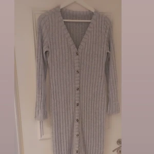 Grå ribbad långklänning från Shein - Säljer en grå ribbad långklänning från Shein i storlek L. Klänningen har v-ringning, långa ärmar och knappar hela vägen framtill. Materialet är mjukt och stretchigt, perfekt för dig som gillar en chill och snygg look.