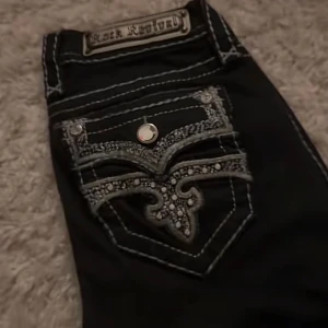 Rock Revival jeans  - Mörk blåa jeans från Rock Revival med grymt snygga broderade detaljer och silvriga nitar på fickorna. Tjocka kontrastsömmar och unika mönster på bakfickan ger en riktigt cool vibe. Jeansen har dragkedja och knapp framtill, och är tillverkade i klassiskt jeansmaterial. Storleken står som 24 men tycker de sitter som 25/26 