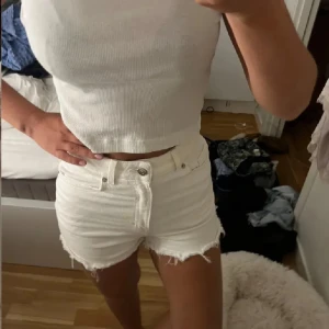Vita jeansshorts - Säljer ett par vita jeansshorts med råa, fransiga kanter. Klassisk femficksmodell med knapp och dragkedja framtill. Perfekta för varma sommardagar och ger en fräsch look till din outfit.