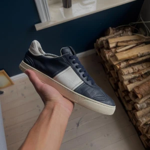 Valentino Flycrew  - Snygga sneakers från Valentino Garavani i mörkblått och vitt skinn. Klassisk låg modell med rund tå, platt sula och snörning. Märkeslogga på plösen och cool kontrast mellan färgerna. Perfekta för dig som gillar stilrena och exklusiva sneakers.👟