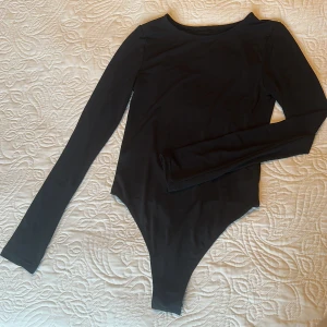 Svart långärmad body med öppen rygg - Säljer en svart långärmad body med rund hals och en stor öppen rygg. Tight passform och tillverkad i stretchigt material. Från NA-KD Josefine HJ kollektion. Använd 1 gång. 