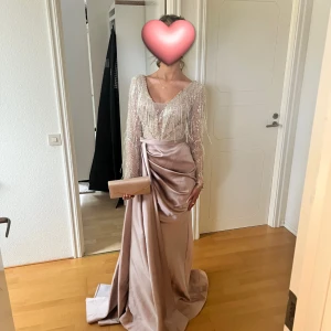 Balklänning i rosé guld - Stl XS/34 - Säljer min otroligt vackra balklänning i färgen rosé guld. Den har en glittrande överdel med pärl- och paljettbroderi samt tunna fransdetaljer som fångar ljuset på ett fantastiskt sätt. Kjolen är i satinliknande tyg med fint fall, en elegant slits framtill och ett litet släp baktill , V ringad och med öppen rygg, perfekt för bal, gala , fest eller bröllop. Klänningen har en lyxig känsla och skimrar i ljuset. Endast använd 1 gång i mycket fint sick , Köpt för 5000 kr säljer nu för 2700kr 