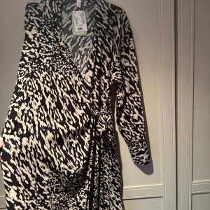Svartvit omlottklänning från H&M (Gravid/Mamma klänning) - Mamma/gravidklänning. Fin svartvit omlottklänning från H&M med v-ringning och knyt i midjan. Klänningen har ett unikt zebramönster och är tillverkad i 100% LivaEco viskos som känns mjuk mot huden. Långärmad och med en snygg krage för extra stilpoäng. Storlek M passar även de som bär S (gravida) passar även efter graviditeten skön fin och flowig. Omlott förkenklar mammalivet. Ny oanvänd med ettikett på. Pris kan diskuteras!