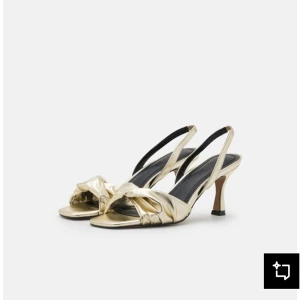 Guldiga sandaler med klack - Säljer ett par snygga sandaler i metallic guld med öppen tå och låg klack. Skorna har en twistad detalj framtill och smala slingback-remmar. Snygg fyrkantig tå och svart innersula. Perfekta för bal och andra evenemang. 