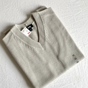 Helt ny stickad väst från Uniqlo - Snygg natural stickad väst från Uniqlo i storlek XS. Västen har v-ringad hals och ribbade kanter vid hals och nederkant. Perfekt att styla över en skjorta eller t-shirt för en clean och chill look.