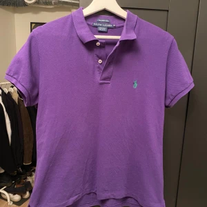 Lila pikétröja från Ralph Lauren, sitter som S-M - Säljer en snygg lila pikétröja från Ralph Lauren i modellen The Skinny Polo. Tröjan har klassisk krage, korta ärmar och två knappar framtill. Ikoniska gröna broderade loggan på bröstet. Tillverkad i 100% bomull för en skön känsla.