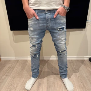 Jack & Jones jeans - Slim fit jeans från Jack & Jones Originals i ljusblå tvätt med slitna detaljer och snygga hål på framsidan. Klassisk femficksmodell med knapp och dragkedja. Jeansen har en smal passform och är tillverkade i mjukt bomullsmaterial med stretch för extra komfort. Jeansen har storleken W30 & L34